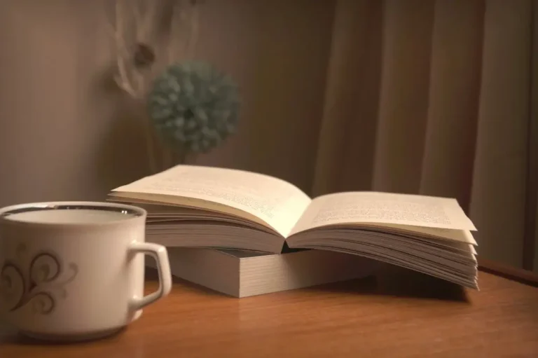 كتاب مفتوح بجانب كوب قهوة على طاولة خشبية بإضاءة دافئة